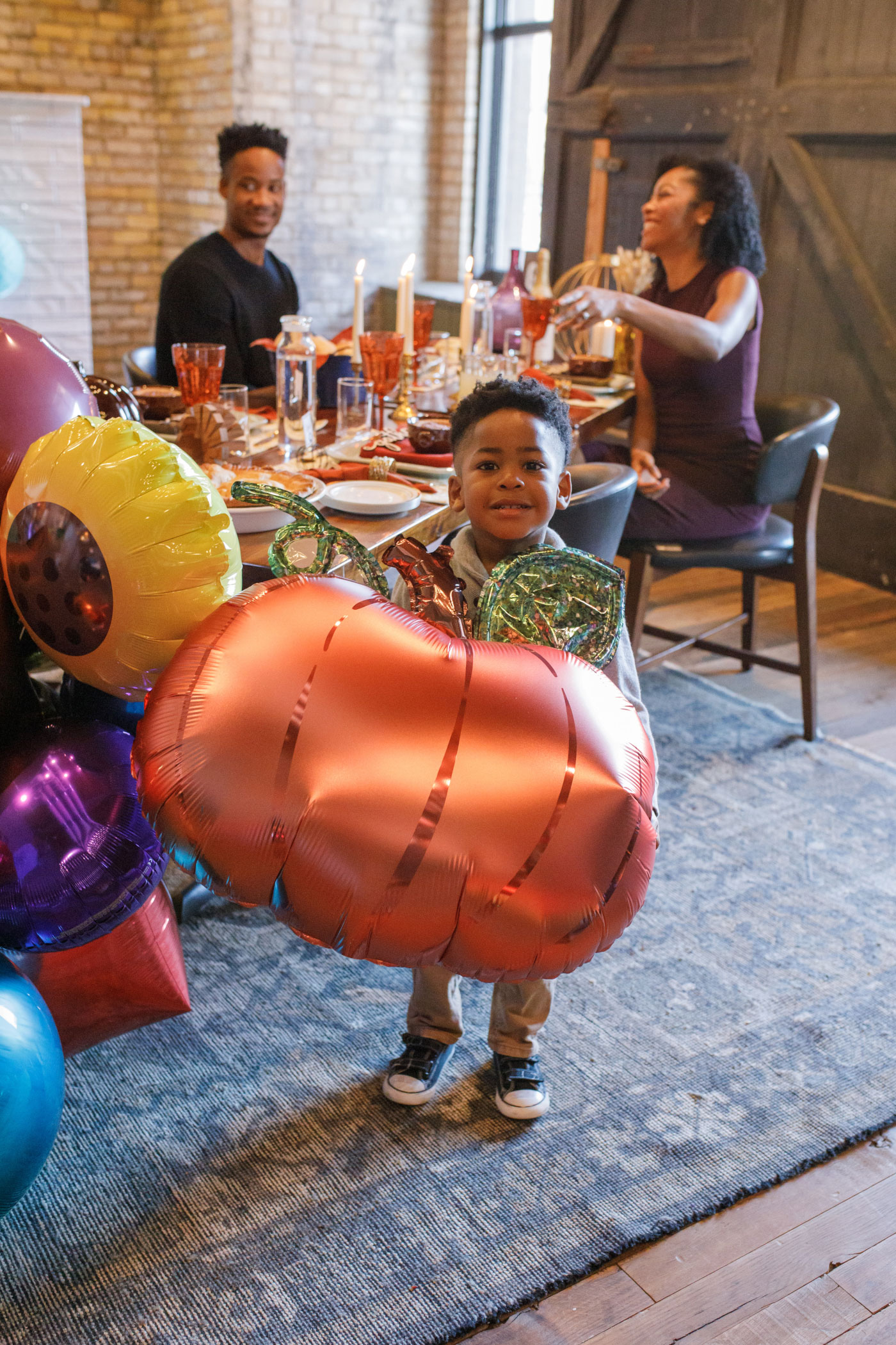 family at thanksgiving party and young boy holding pumpkin balloon